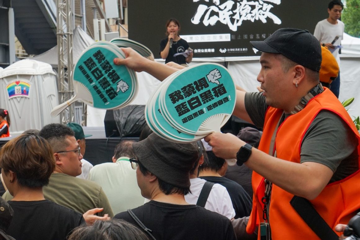 A volunteer hands out fans with a slogan saying, “I despise the white and blue camps and their blackbox politics.”