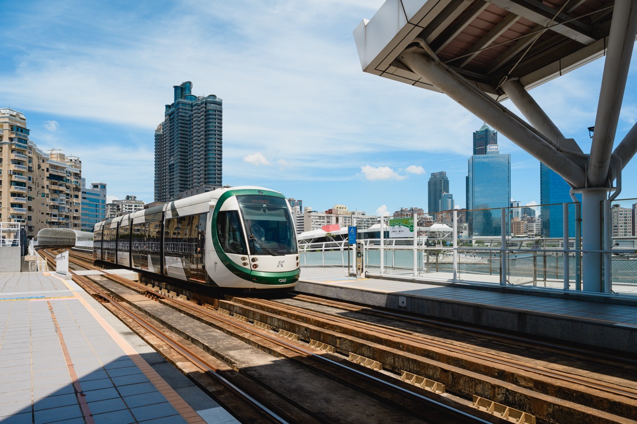 A light rail train passes the Port of Kaohsiung, with the city's skyline in the background.